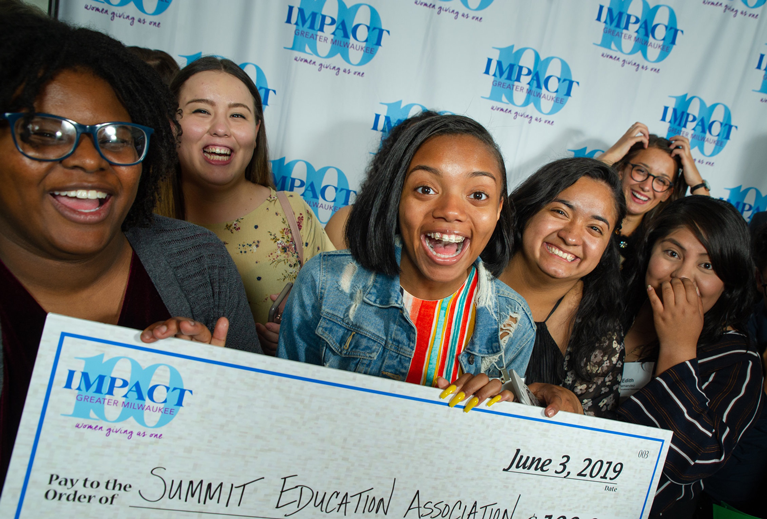 Women excitedly hold an oversized check